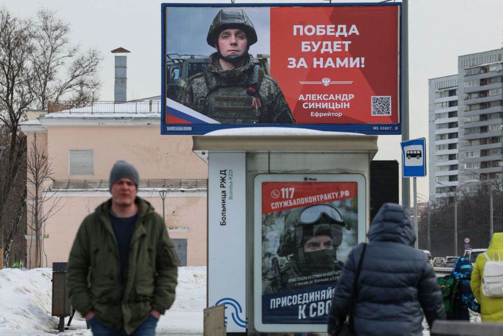 Здымак мае ілюстрацыйны характар. Людзі праходзяць ля рэкламнага шчыта ў гонар расейскага вайскоўца і плаката на прыпынку грамадскага транспарту, які рэкламуе кантрактную службу ў войску. Масква, Расея. 26 лютага 2024 года. (Фота: Vera Savina / AFP / EAst News)