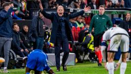 Trener Niels Frederiksen, stoi na boisku piłkarskim z otwartymi ustami, wyrażając wściekłość lub frustrację, w tle widać rozmazanych ludzi i trybuny stadionu.