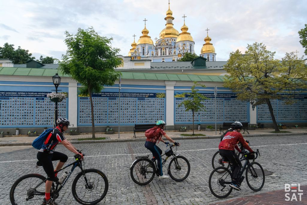 Здымак мае ілюстрацыйны характар. Раварысты праязджаюць міма Сцяны памяці з фотаздымкамі ўкраінскіх вайскоўцаў, якія загінулі ў вайне з расейскімі войскамі з 2014 года. Кіеў, Украіна. 28 траўня 2024 года. (Фота: Уладзіслаў Максіменка / Белсат)