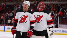 Na zdjęciu widzimy dwóch zawodników New Jersey Devils tuż po zakończeniu emocjonującego spotkania z Chicago Blackhawks. Ubrani w białe wyjazdowe stroje z charakterystycznym czerwono-czarnym logo, stoją na lodzie w otoczeniu kibiców, którzy wypełniają trybuny hali. Po lewej stronie znajduje się gracz z pola, trzymający kij hokejowy i noszący rękawice marki Warrior, po prawej bramkarz z numerem 25 na kasku, wyposażony w zestaw ochronny. Ich postawa i spojrzenia sugerują chwilę ulgi (fot. Getty Images)