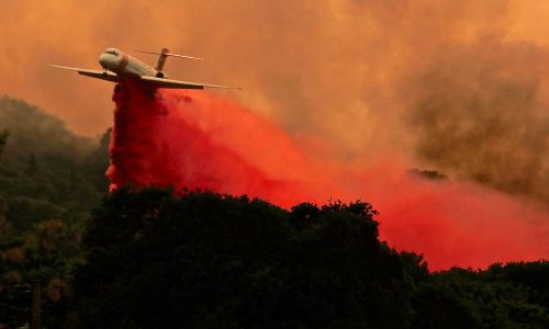 USA, 29 lipca 2018 r. Samolot przeciwpożarowy zrzuca porcję środka mającego spowolnić ogień Fire River, części wielkiego skupiska pożarow Mendocino Complex Fire w Lakeport w Kaliforni. Dwa jego ogniska – River Fire i Ranch Fire –  razem pochłonęły 22 660 hektarów, powiększając spalony teren prawie dwukrotnie od niedzieli. Ponad 10 000 osób zostało już ewakuowanych z tych terenów. Fot. PAP/EPA / ALAN SIMMONS