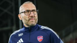 Marek Papszun w ciemnym sportowym stroju z emblematem Rakowa Częstochowa i inicjałami „MP” stoi na tle stadionowego oświetlenia, skupiony i wyciszony. Jego sylwetka, wyraz twarzy i profesjonalny ubiór podkreślają trenerski autorytet oraz gotowość na nowe wyzwania. W kontekście medialnych doniesień o możliwym objęciu posady w Norwich City, fotografia nabiera symbolicznego znaczenia — to moment przejściowy, w którym polski szkoleniowiec może wkroczyć na angielską scenę piłkarską (fot. Getty Images)